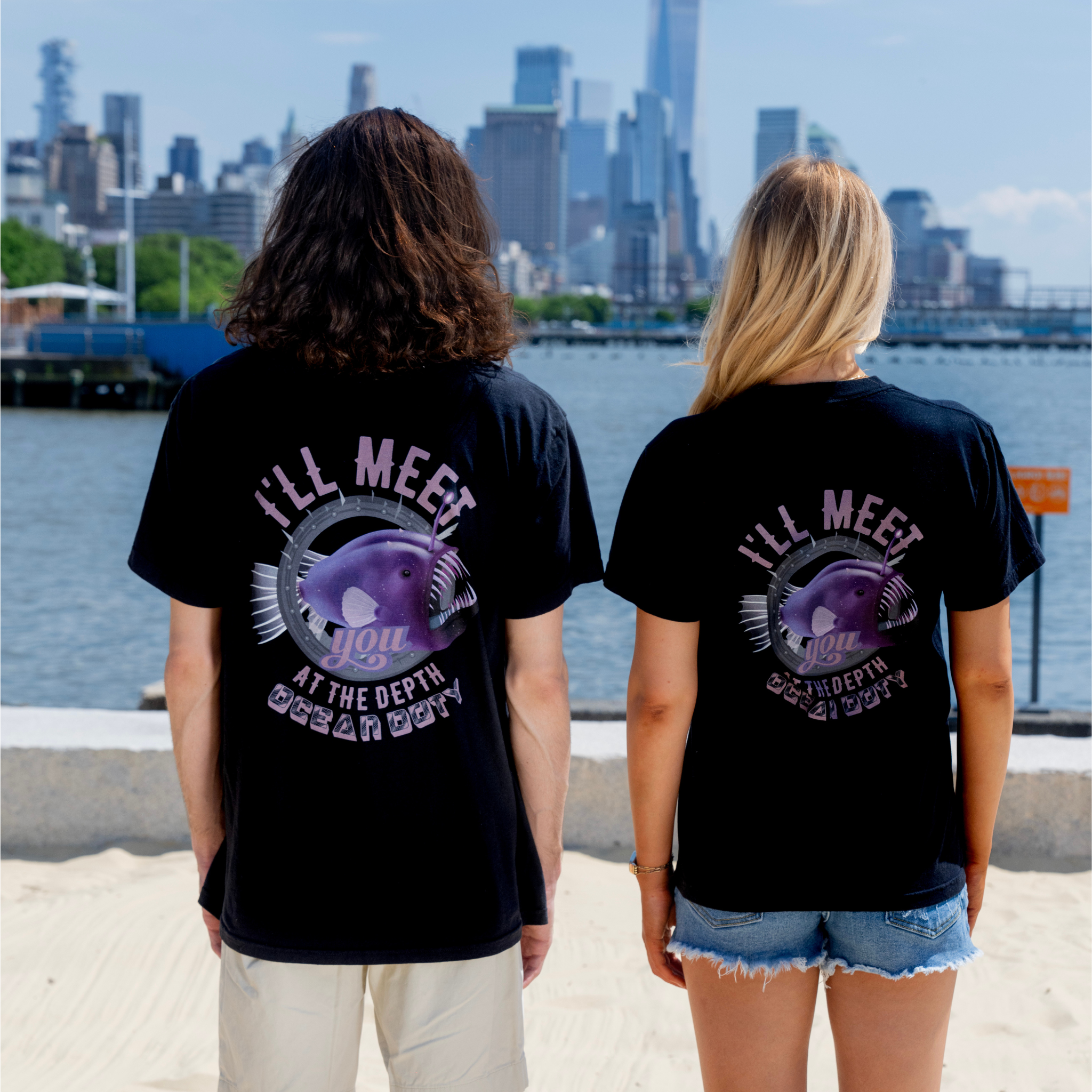 Two people wearing black t-shirts with a vibrant purple deep sea fish referring to the ocean's depth.