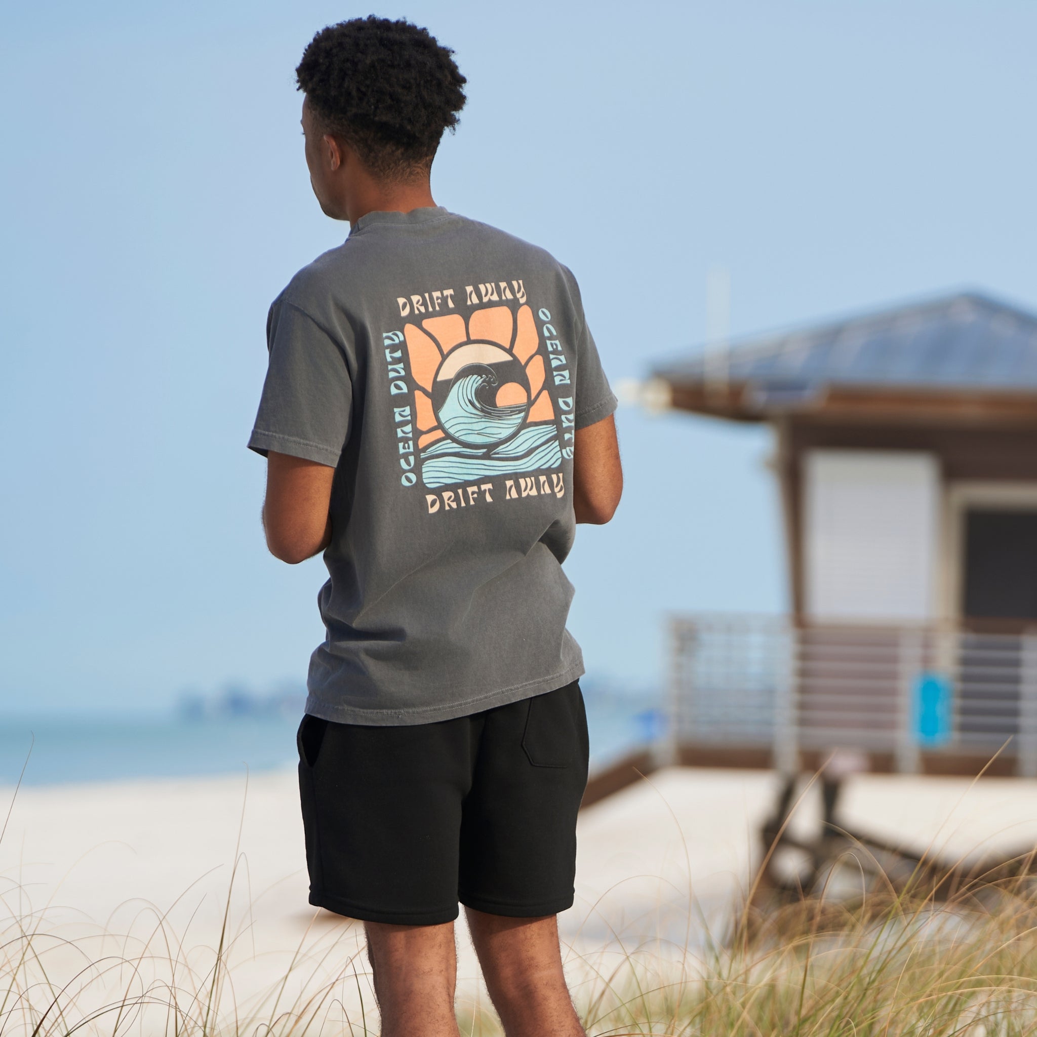 Man wearing a faded black t-shirt with graphic print of a ocean wave and the words 'drift away.'