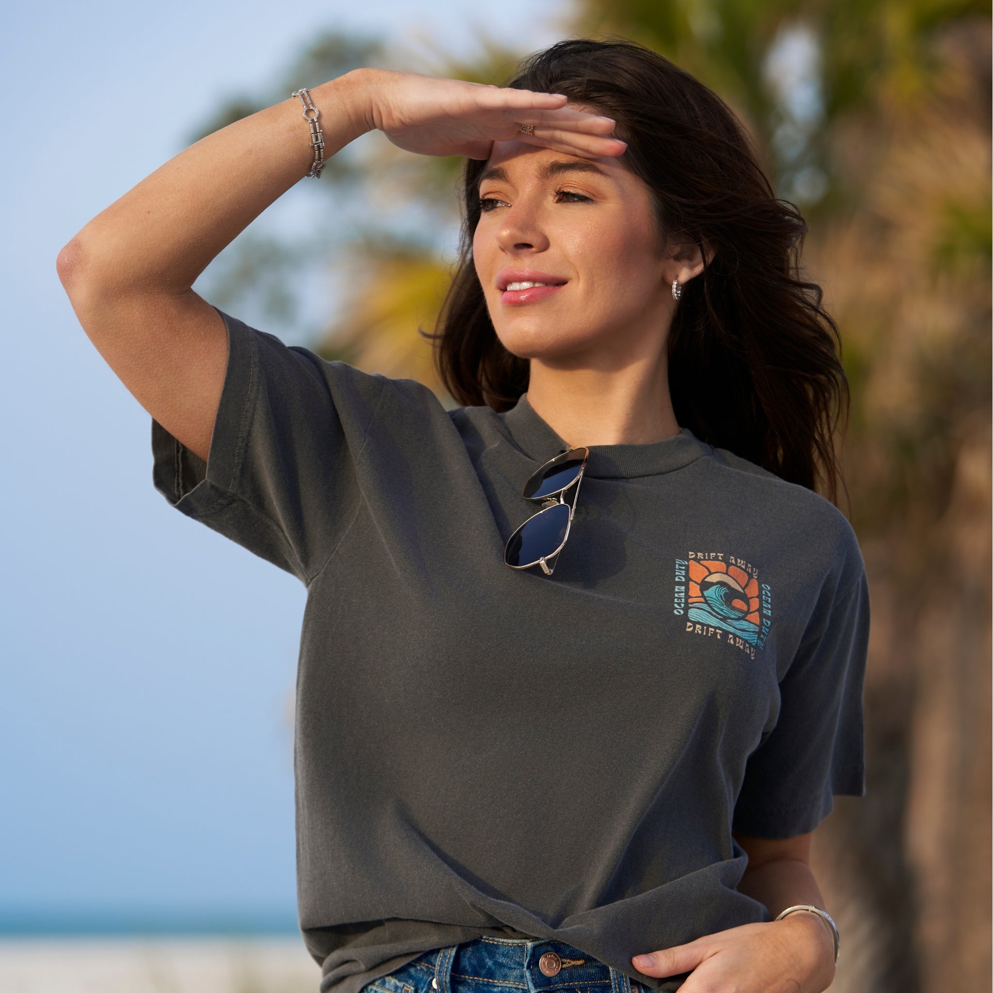 A woman wearing a faded black t-shirt with graphic print of a ocean wave and the words 'drift away.'