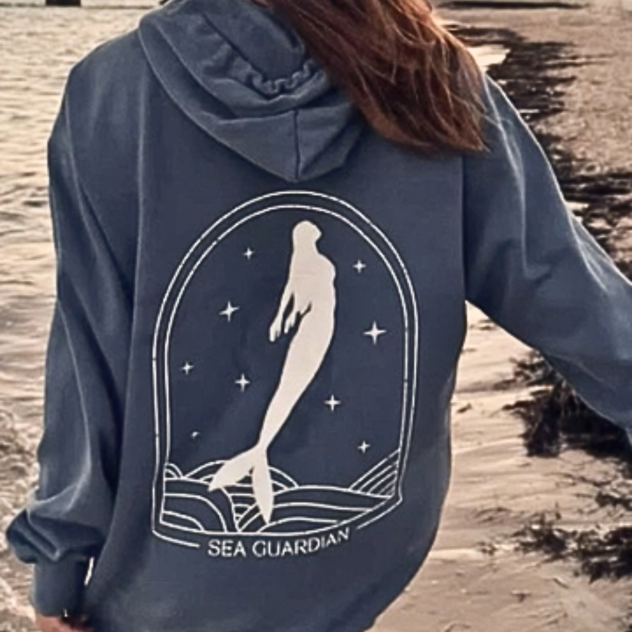 Navy blue hoodie with mermaid design and 'Sea Guardian' text on a beach.