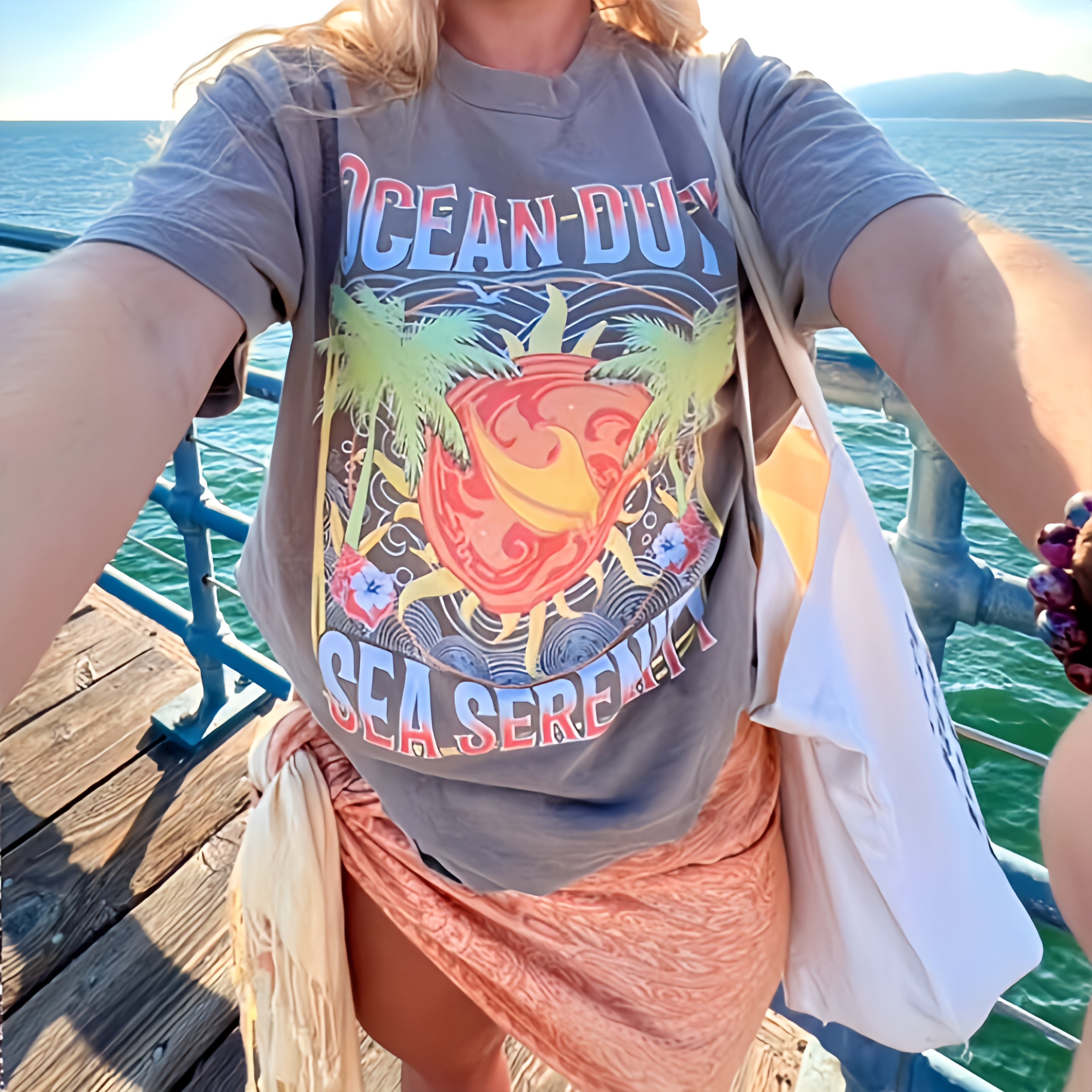 Person wearing a t-shirt with 'Ocean Duty Sea Serenity' design on a dock by the water.