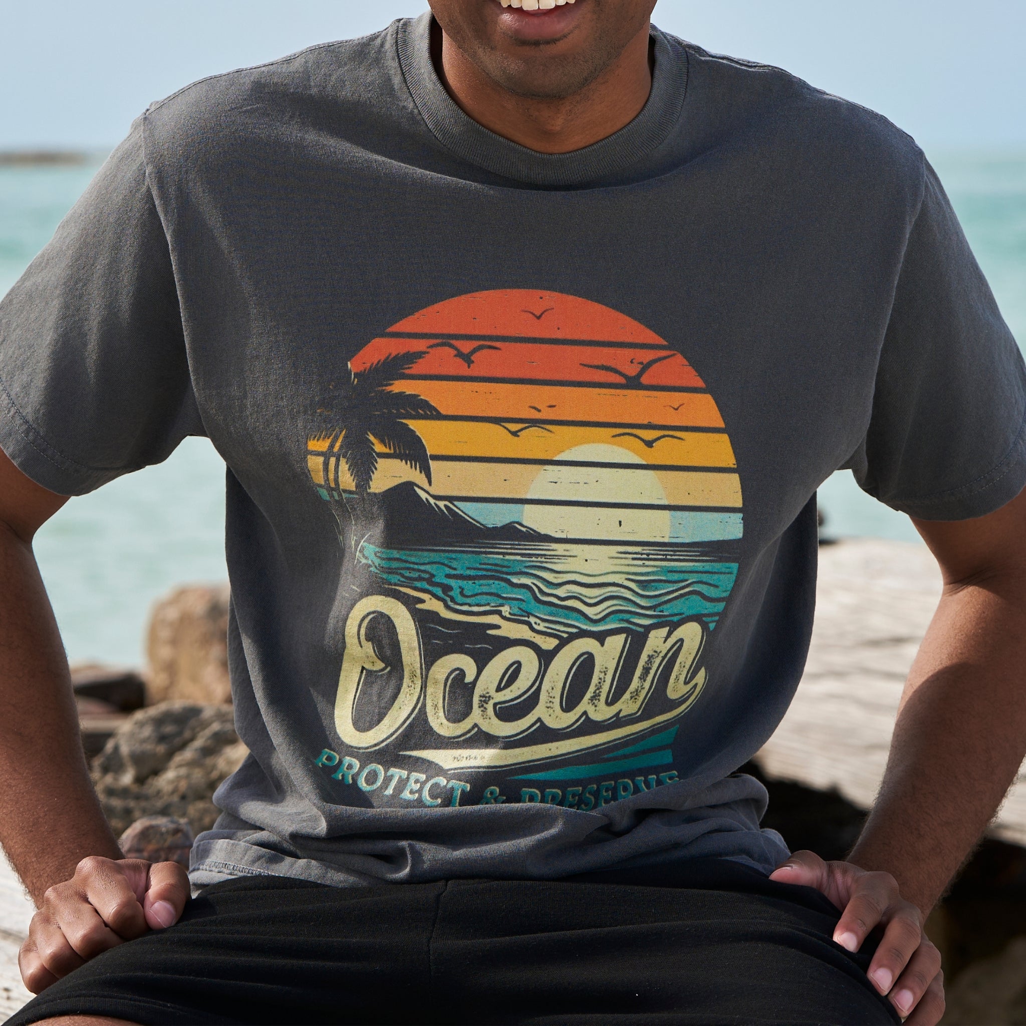 A man wearing a faded black t-shirt with an ocean sunset over a beach with the words 'protect & preserve' printed below.'