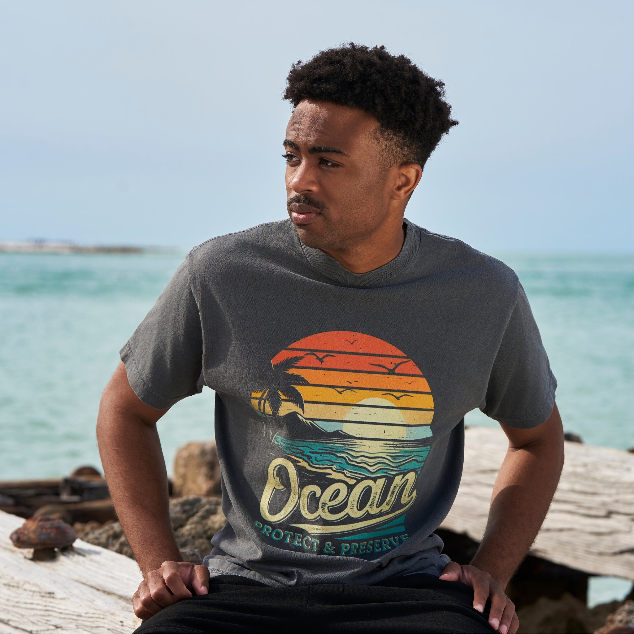 A man on the beach wearing a faded black t-shirt with an ocean sunset over a beach with the words 'protect & preserve' printed below.'