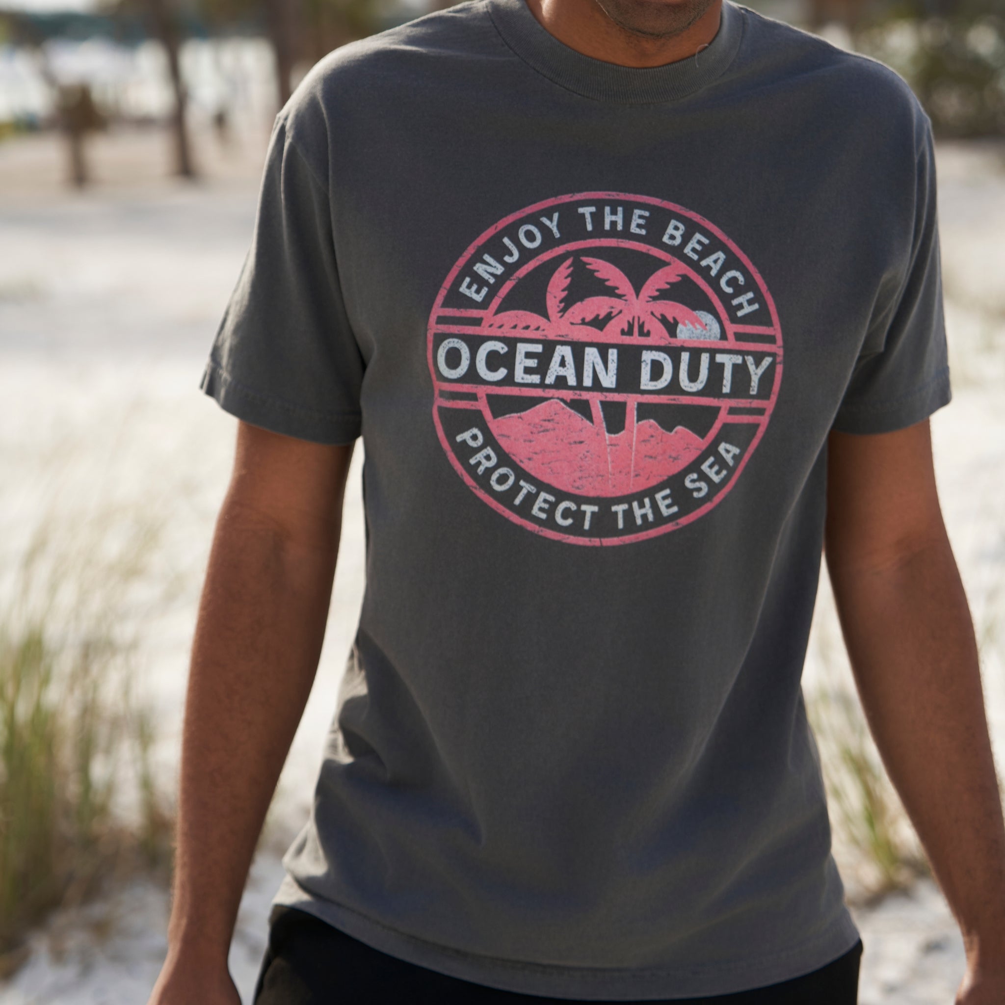 A man wearing a faded black T-shirt with a red and white tropical beach graphic design printed on the front about ocean conservation.