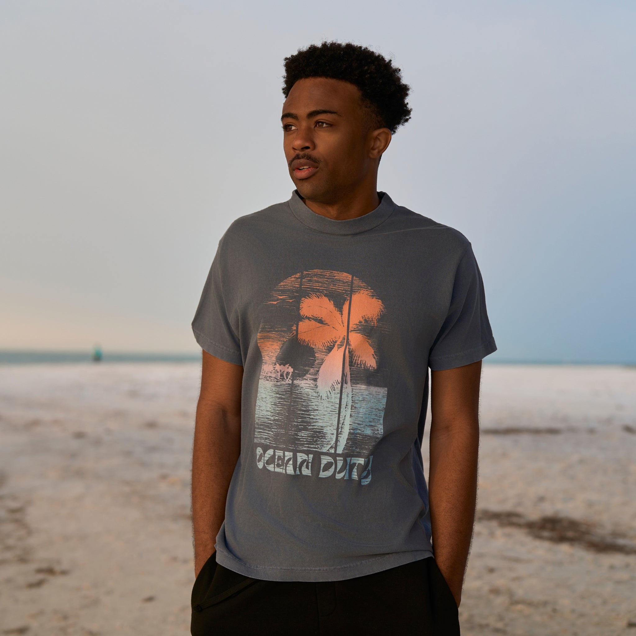 A male  wearing a faded Blue T-shirt with colorful tropical graphic print on the front.