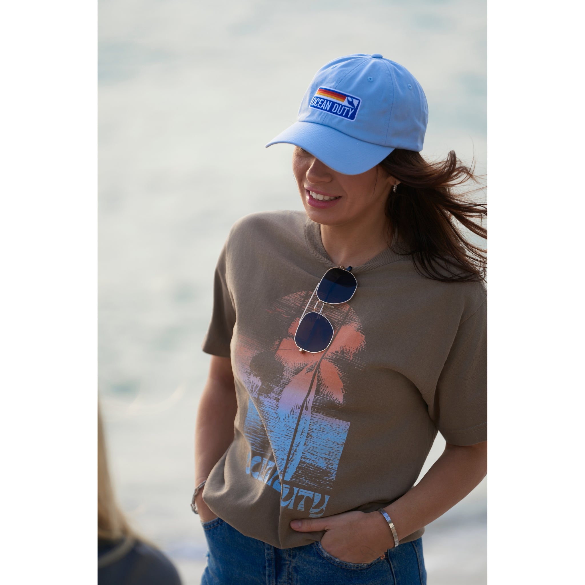 A woman wearing a faded brown T-shirt with distressed colorful beach print on the the front, and a dad cap.