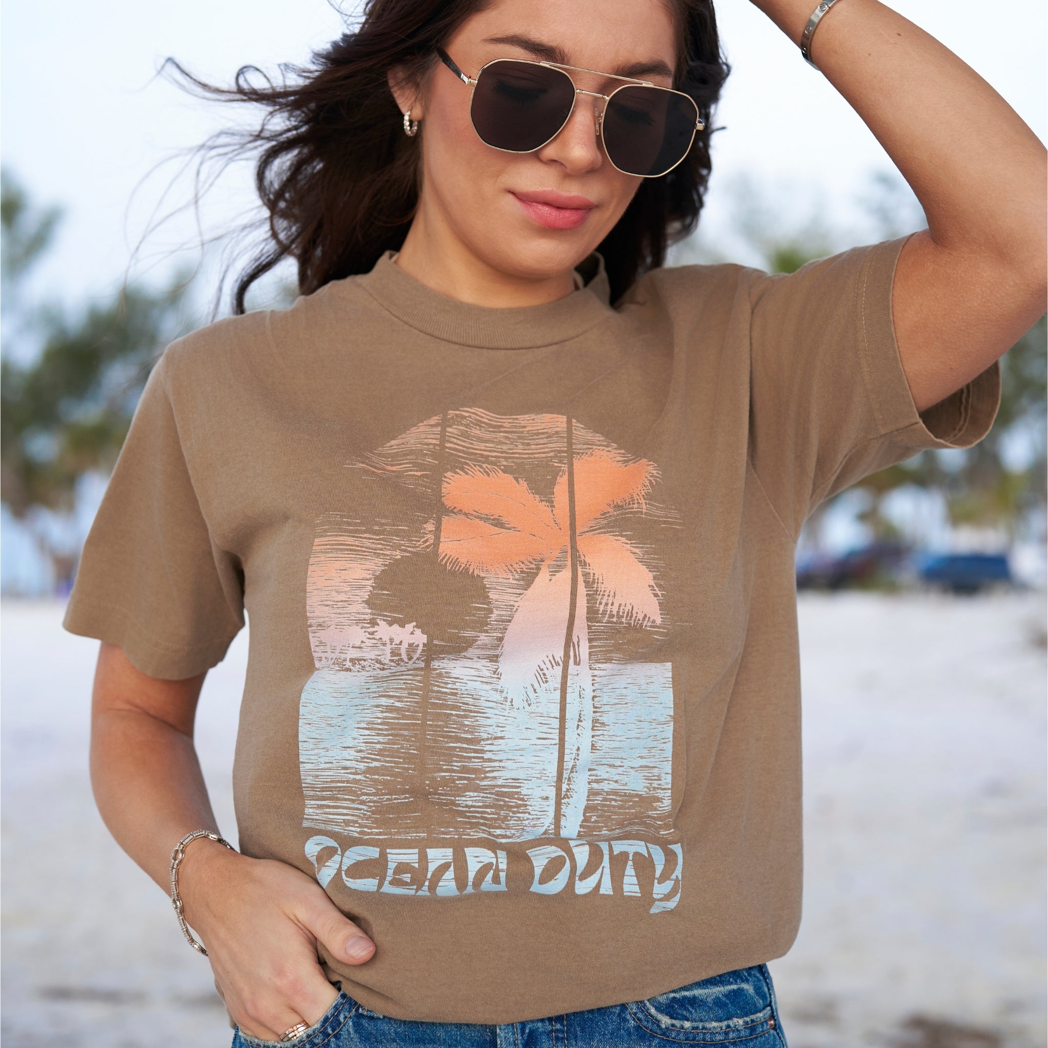 A woman wearing a faded brown T-shirt with distressed colorful beach print on the the front.
