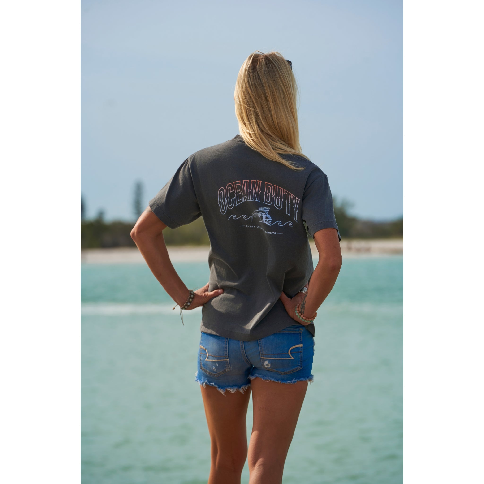 A woman on a beach wearing faded black T-shirt that has an ocean fish graphic.