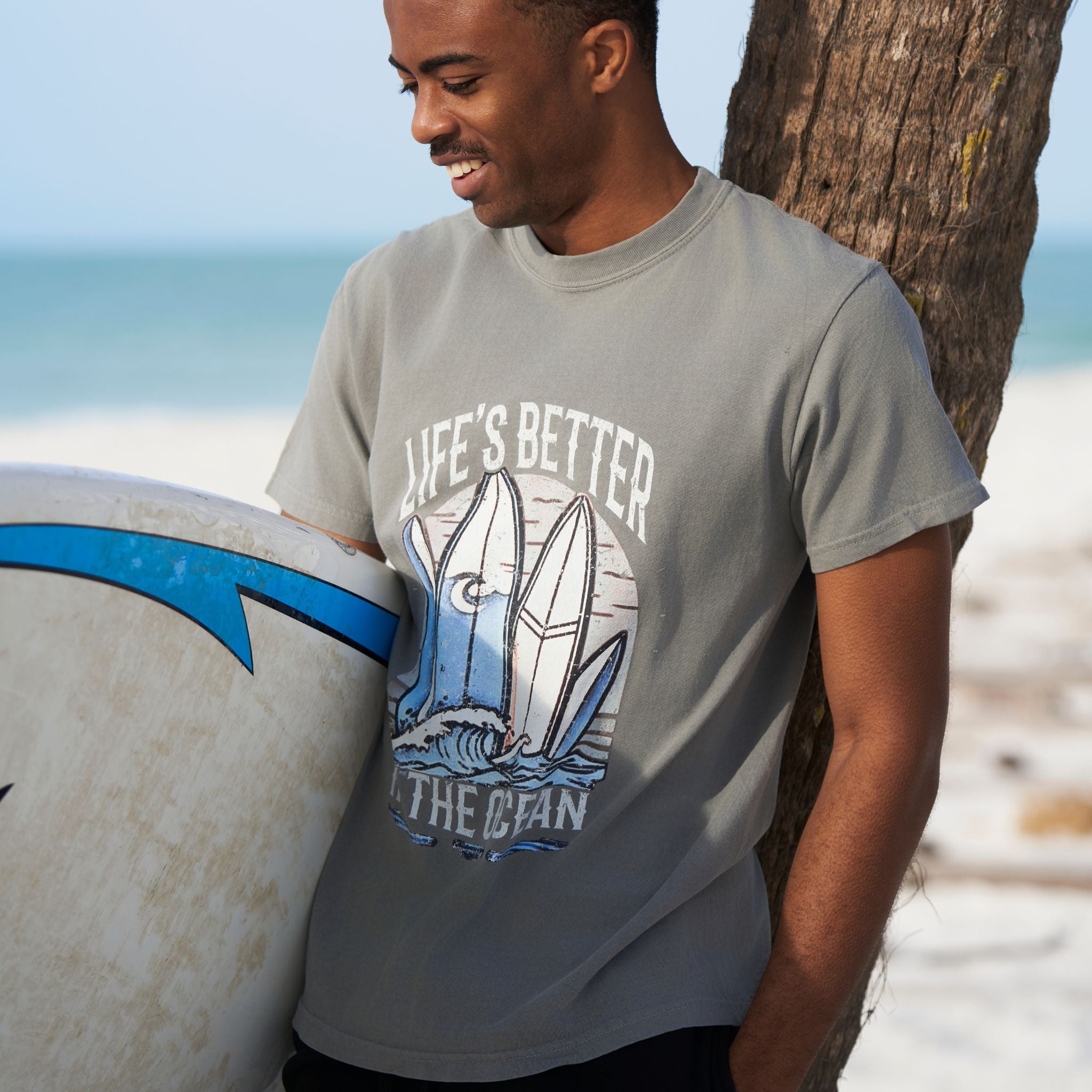 Man at the beach wearing a grey T-shirt that has a graphical picture of surfboards on the ocean.