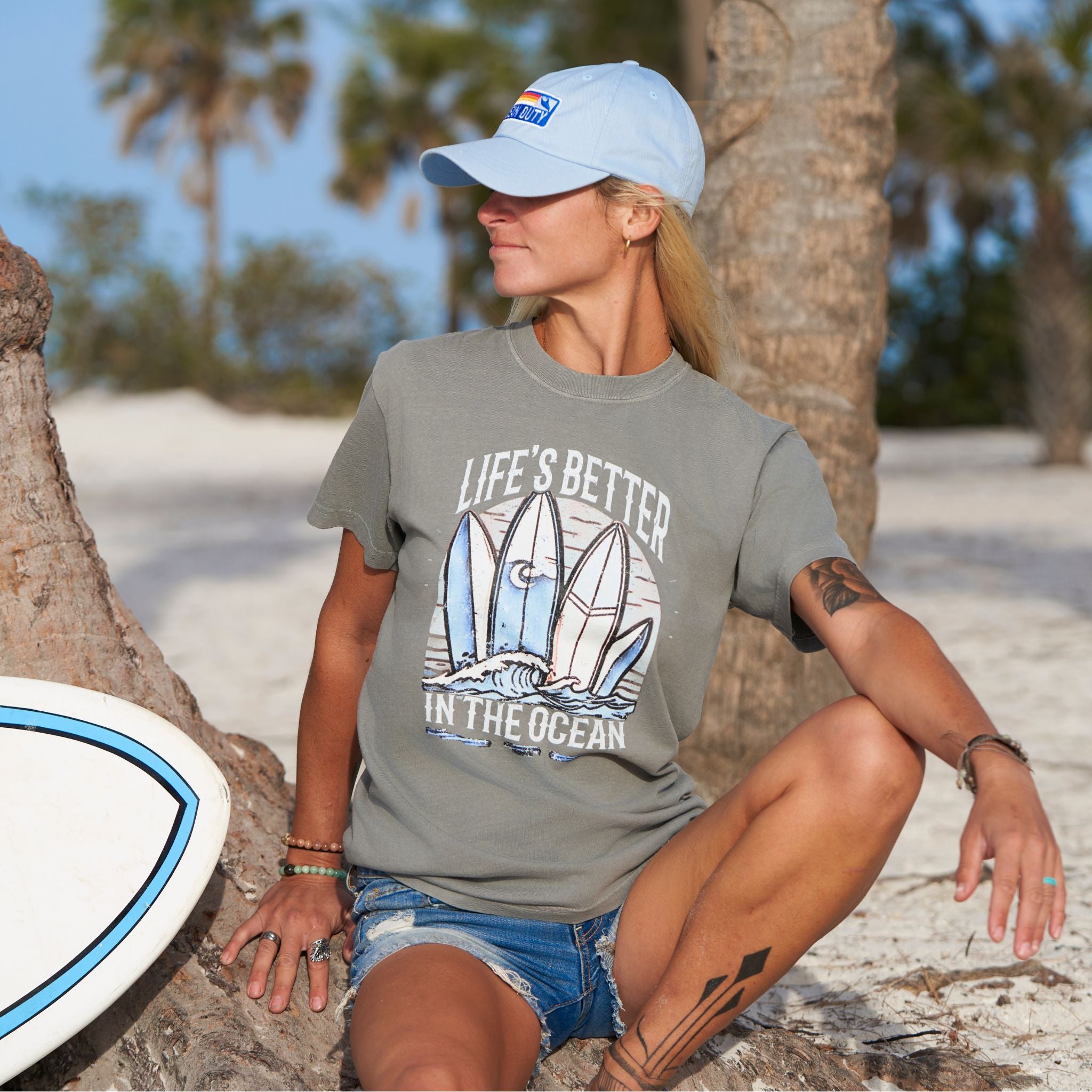 Woman at the beach wearing a grey T-shirt that has a graphical picture of surfboards on the ocean.