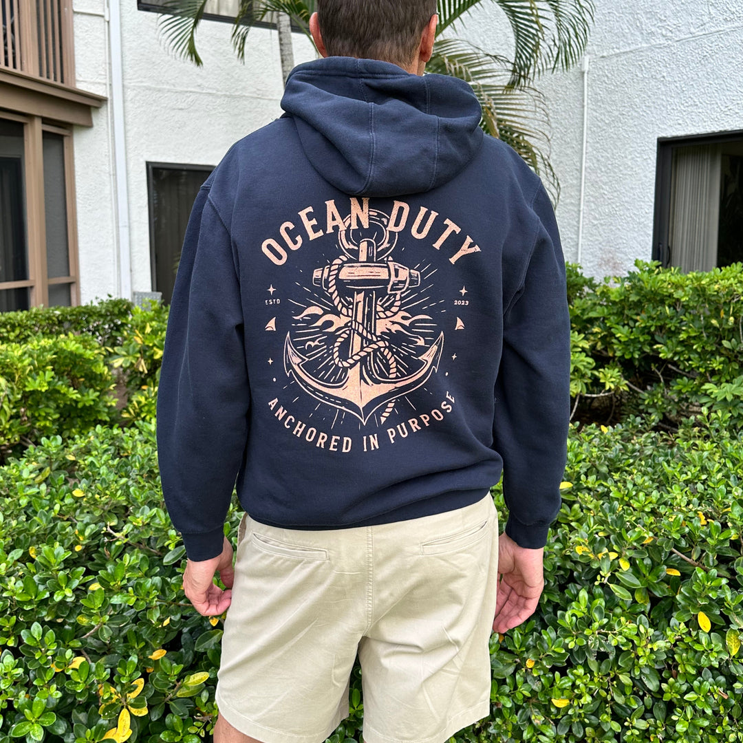A man viewed from behind wearing a navy blue hoodie with a large anchor graphic and the words &