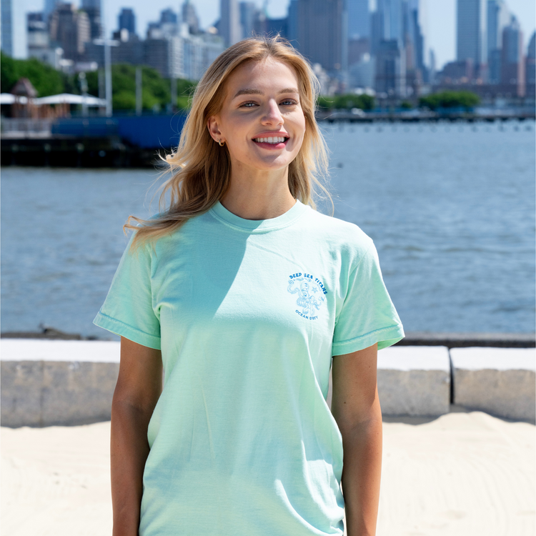 A woman wearing a light green t-shirt with a graphical picture of an octopus and print 'deep sea titans.'
