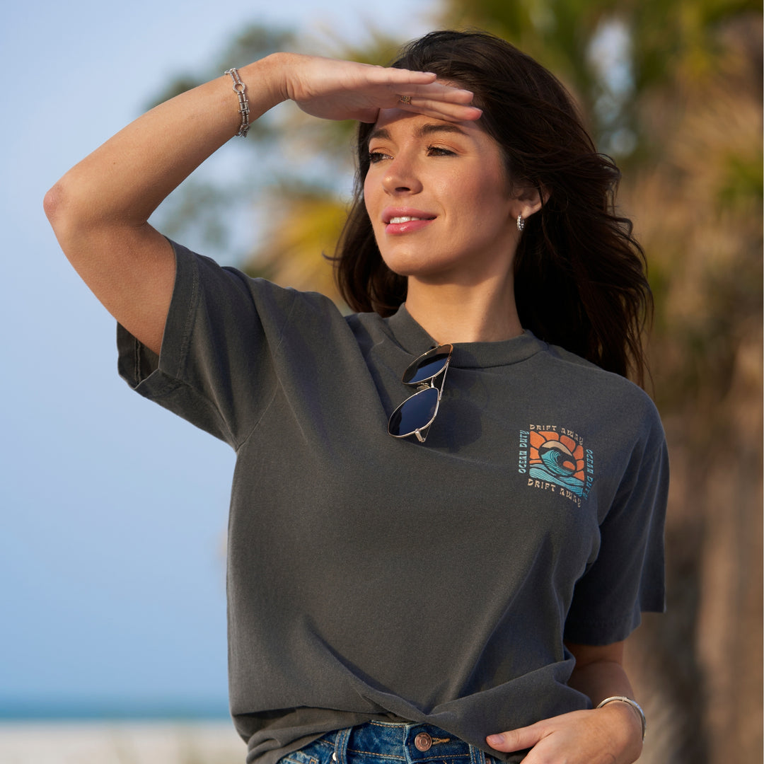 A woman wearing a faded black t-shirt with graphic print of a ocean wave and the words 'drift away.'