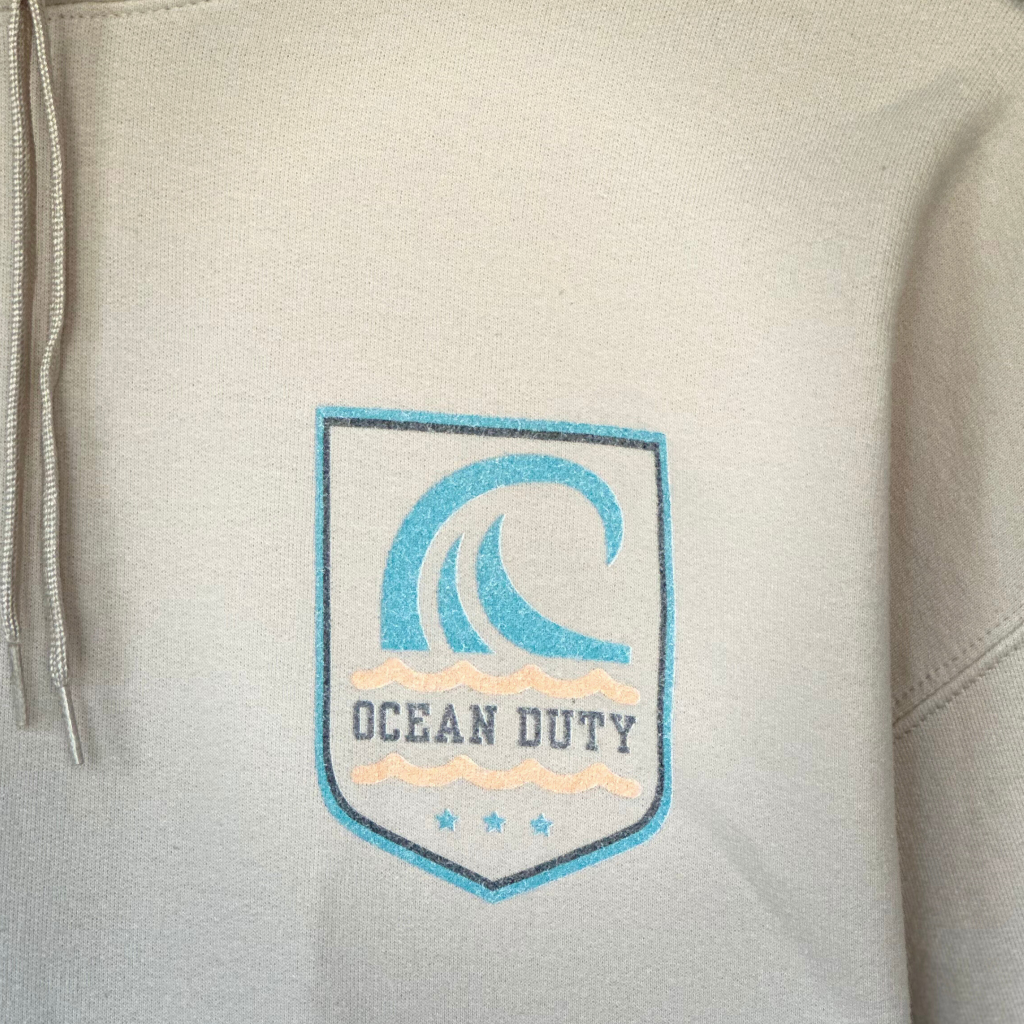 Close up graphic on a sand colored hoodie with large wave graphic on back