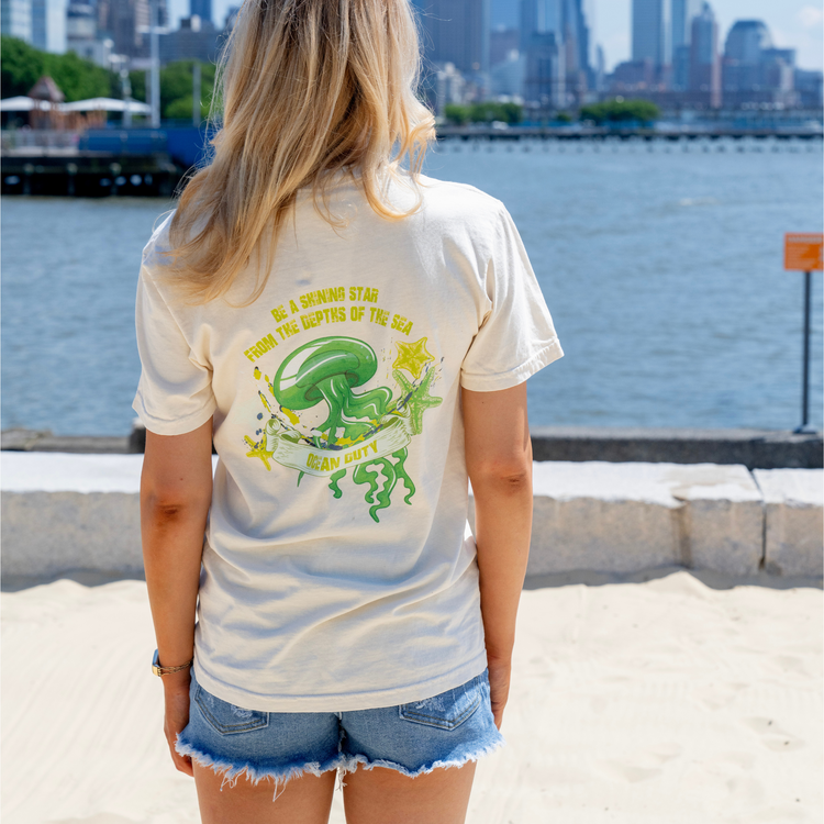 A woman wearing an ivory t-shirt with a bright green jellyfish graphic and print on the back.