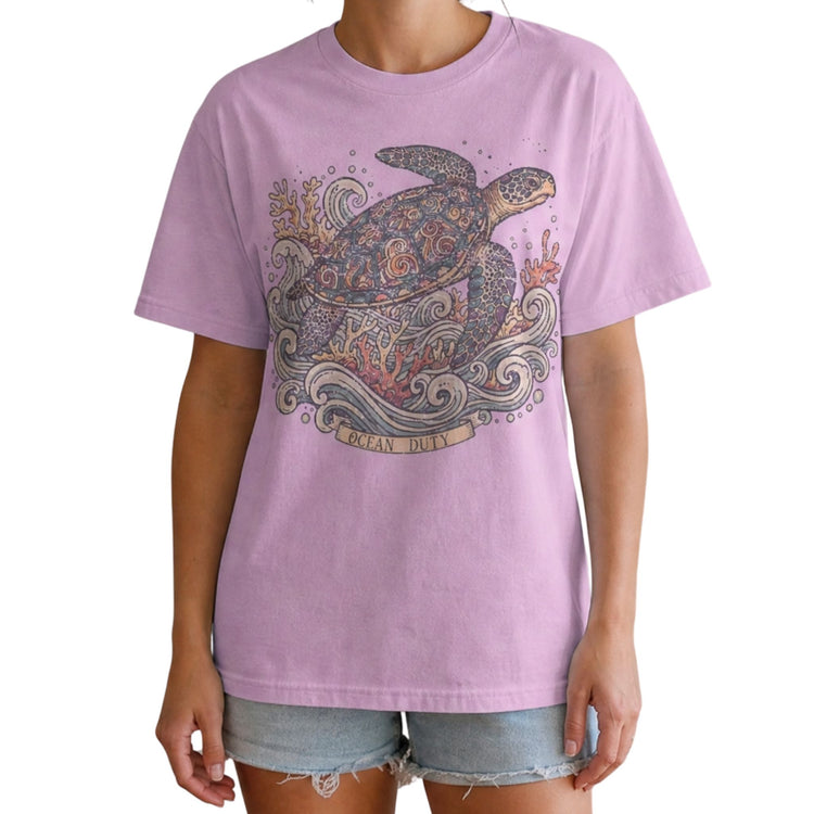 A model wearing a lavender short-sleeve t-shirt with a detailed graphic of a sea turtle, starfish, and waves on the front, paired with denim shorts against a plain white background.