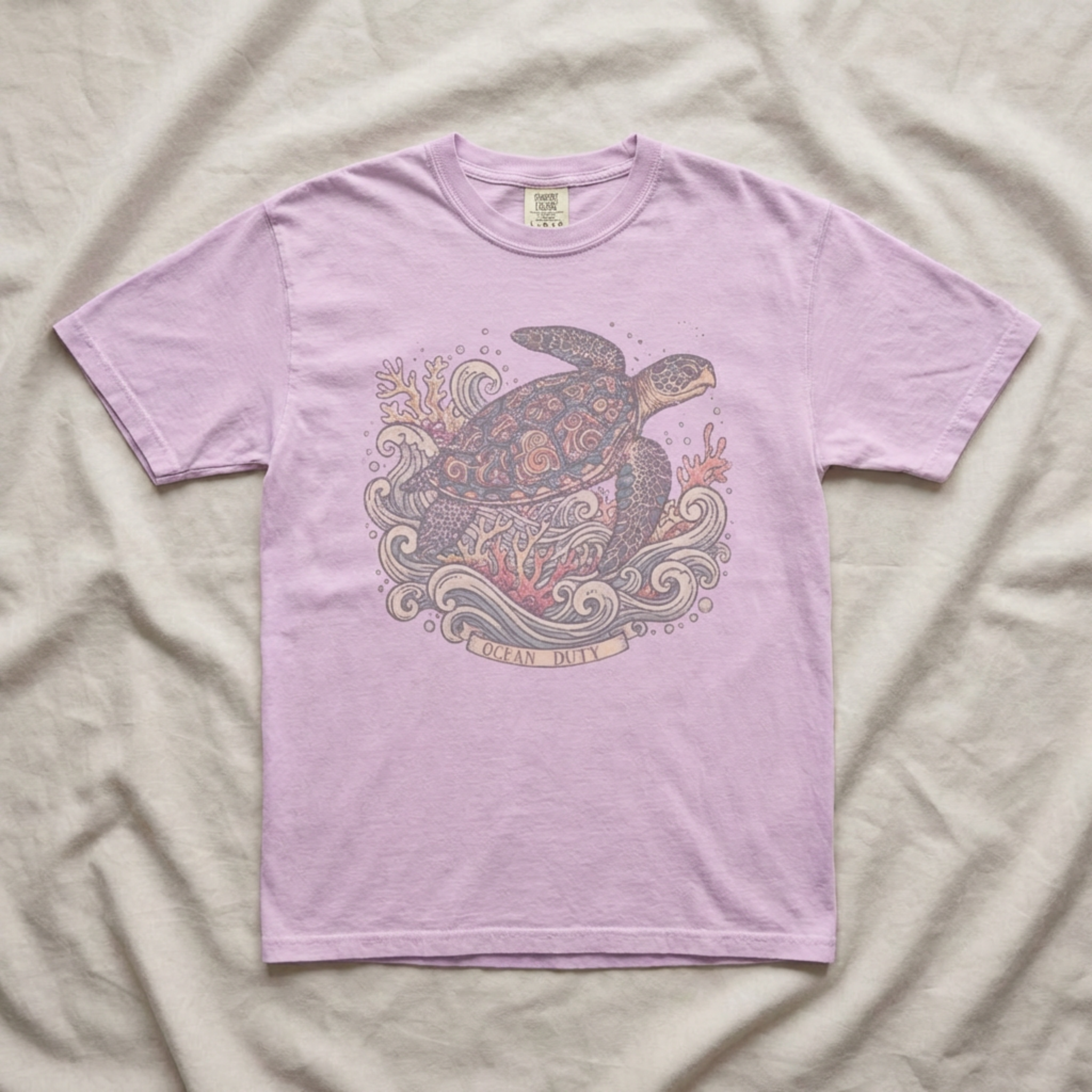 A light purple short-sleeve t-shirt with a detailed turtle graphic on the front, laid flat on a beige fabric background.