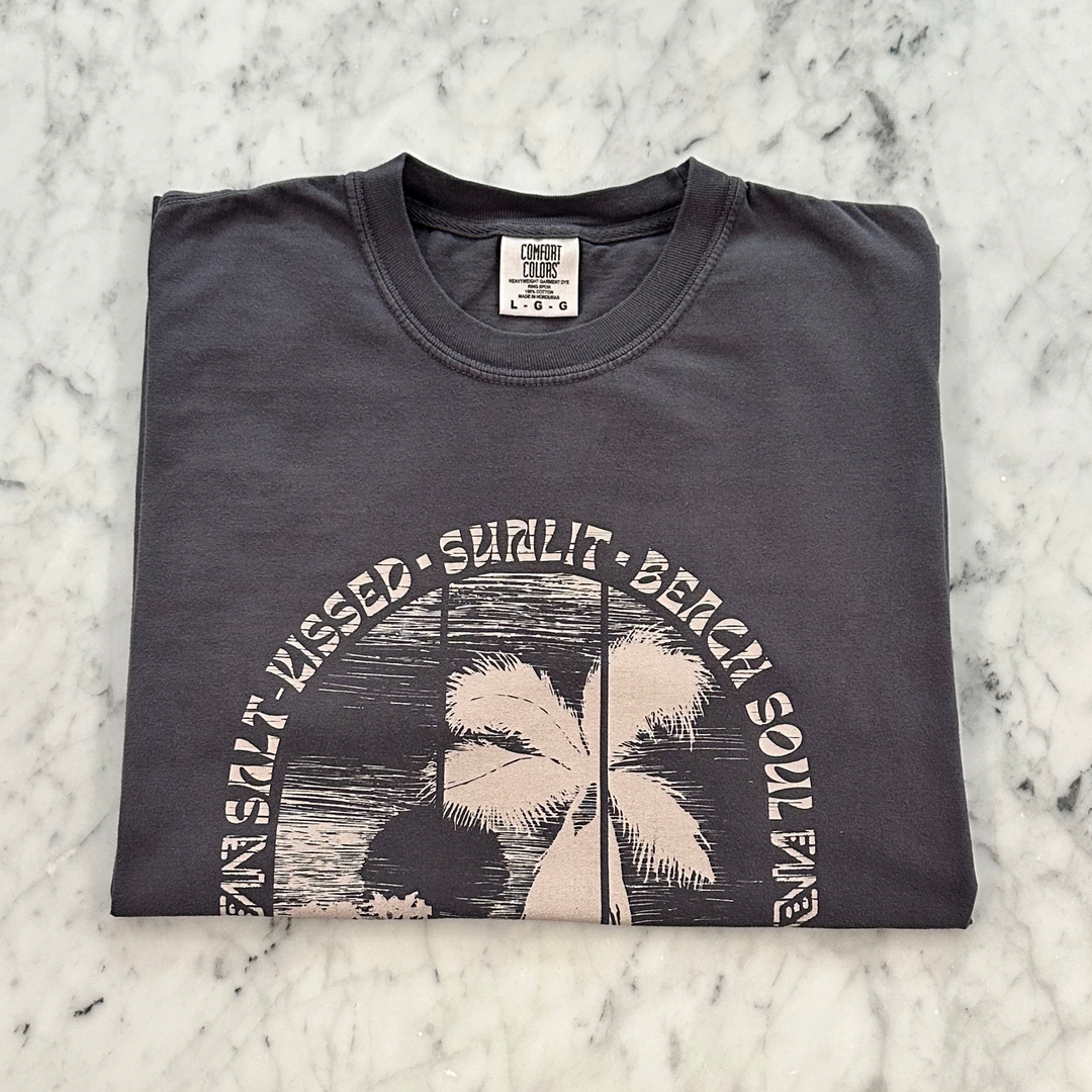 A folded dark charcoal gray t-shirt with a vintage-style palm tree graphic and the text &